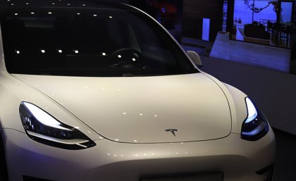 A futuristic Tesla car sits in a showroom with blue lights in the background